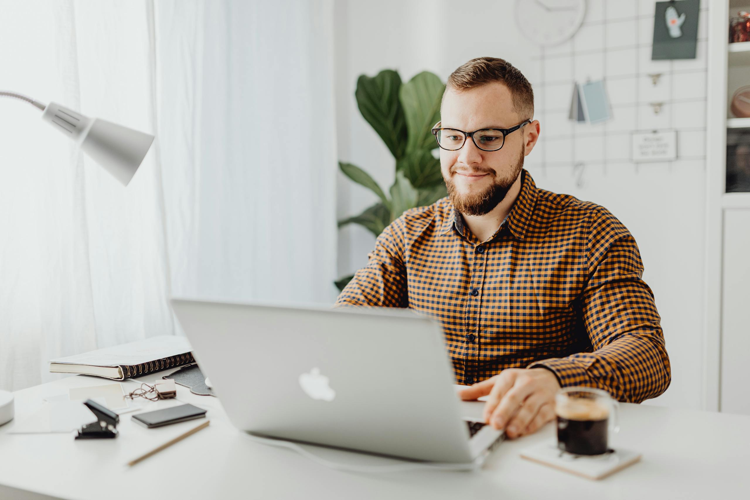Adult man with eyeglasses typing on a laptop in a modern home office setting.